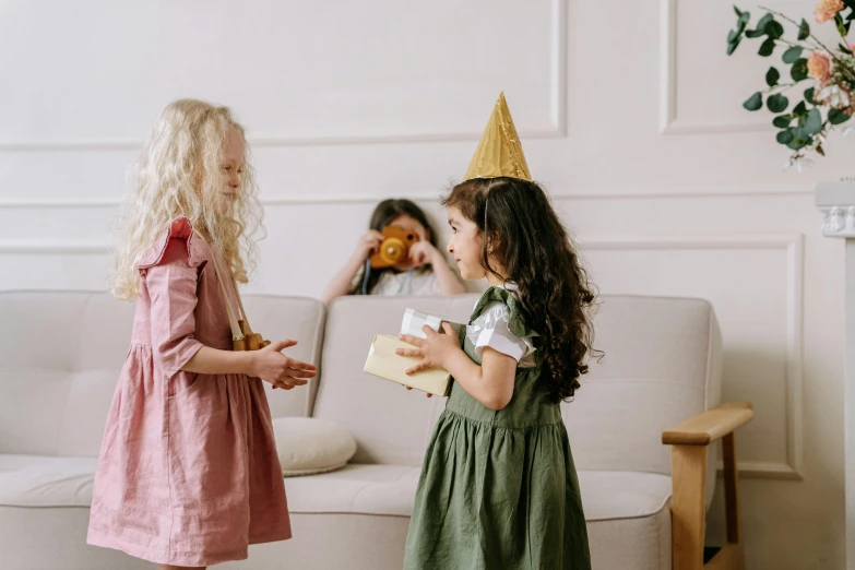 two little girls standing next to each other on a couch, pexels contest winner, happening, party hats, smiling at each other, background image, decoration around the room