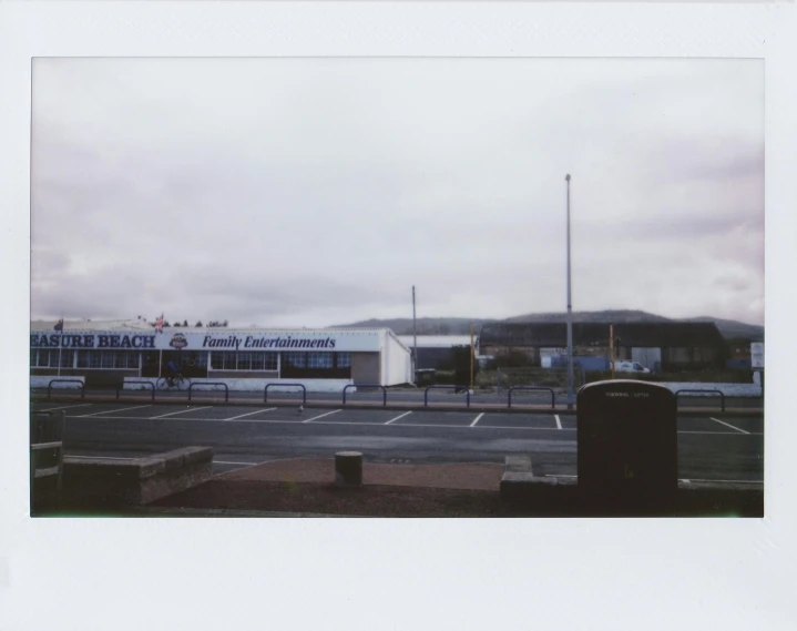 a bus parked in a parking lot next to a building, a polaroid photo, stadium landscape, at the seaside, vhs colour photography, digital photograph