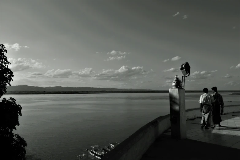 a couple of people standing next to a body of water, a black and white photo, by Altichiero, panoramic anamorphic, eyelevel!!! view!!! photography, taken at golden hour, on a pedestal