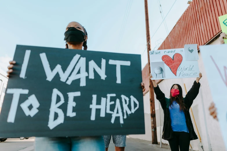 a woman holding a sign that says i want to be heard, by Julia Pishtar, trending on pexels, protesters holding placards, ears, new mexico, view from the streets