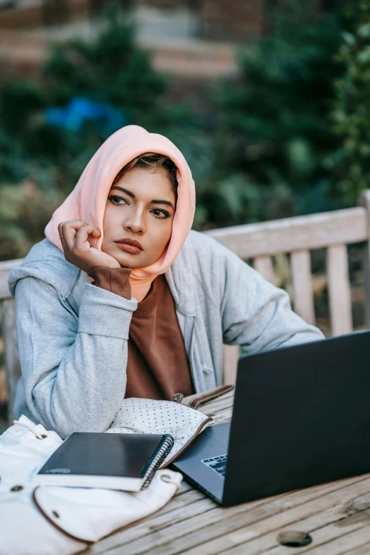 a woman sitting at a table with a laptop, a colorized photo, inspired by Maryam Hashemi, trending on pexels, hurufiyya, bashful expression, in a park, looking serious, student