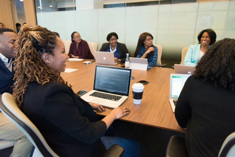 a group of people sitting around a table with laptops, by Malvin Gray Johnson, pexels contest winner, cubical meeting room office, photo of a black woman, profile picture, ground level shot