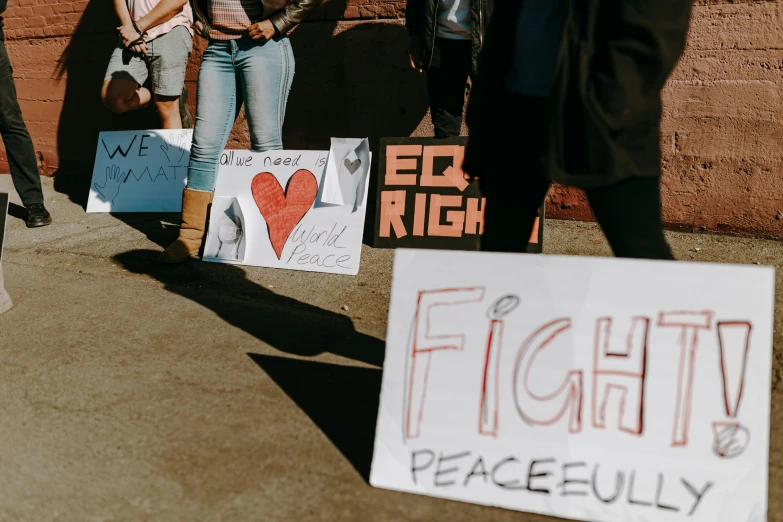 a group of people standing in front of a brick wall, trending on pexels, graffiti, protesters holding placards, peach, world peace, high school