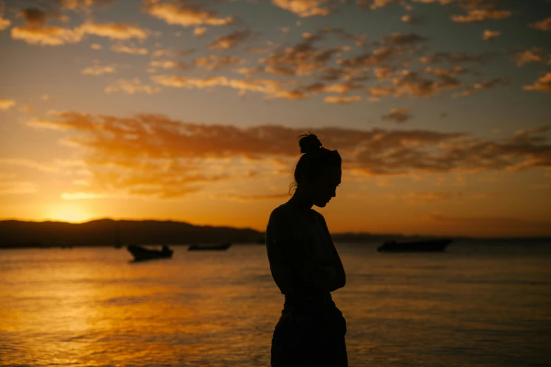 a woman standing on top of a beach next to the ocean, pexels contest winner, sunset glow around head, sad expression, silhouettes, manly