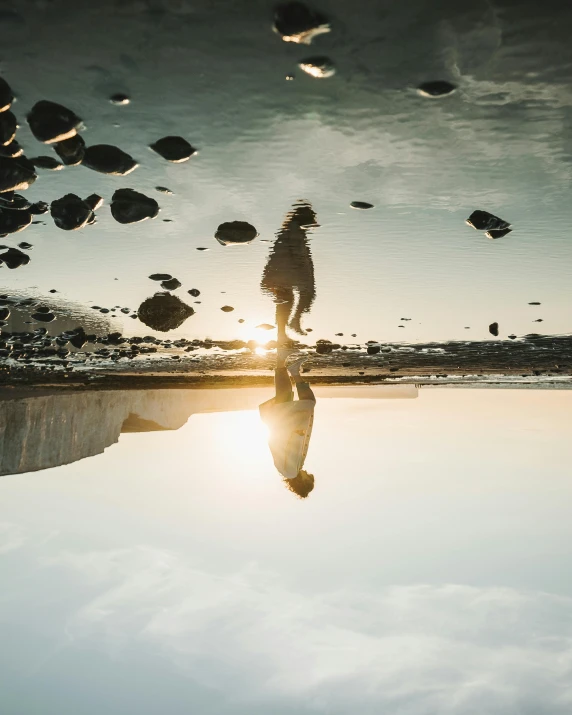 a person standing in front of a body of water, by Christen Dalsgaard, unsplash contest winner, surrealism, sun puddle, stones falling from the sky, admiring her own reflection, floating in mid - air