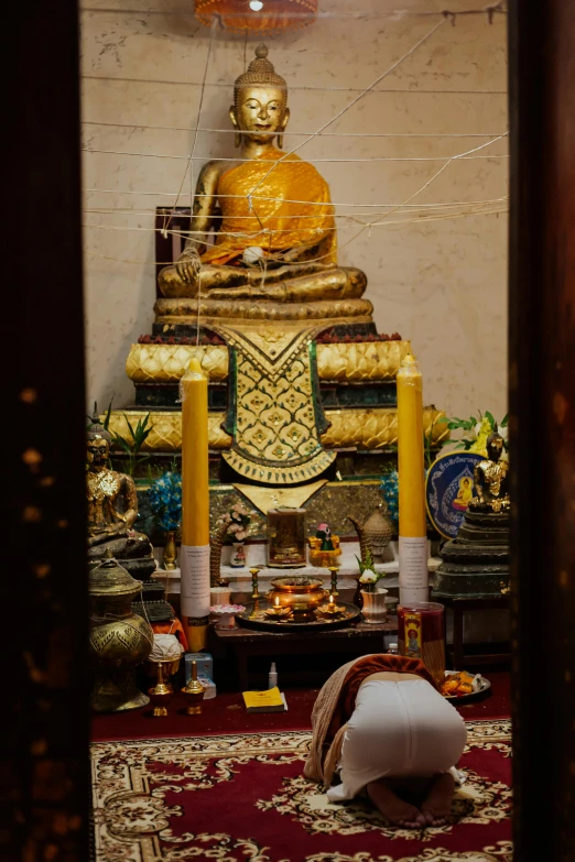 a person kneeling on the ground in front of a statue, unsplash, an altar of a temple, gold decorations, laos, inside building