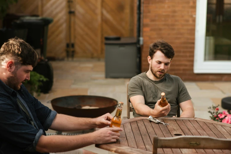 a group of men sitting around a wooden table, by Nick Fudge, pexels contest winner, holding a bottle, sitting in the garden, profile image, annoyed