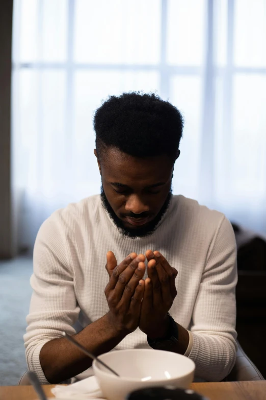 a man sitting at a table praying, pexels contest winner, man is with black skin, recovering from pain, gray men, mkbhd