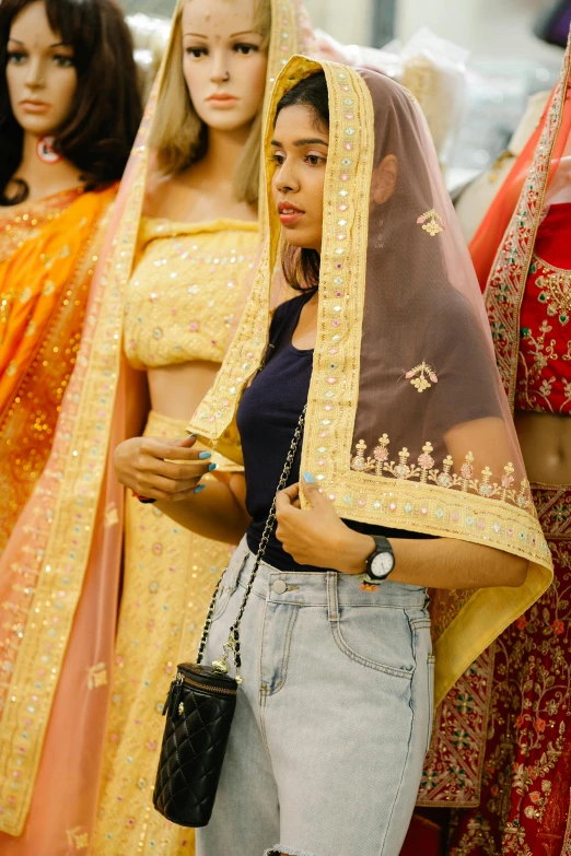 a woman standing in front of a group of mannequins, pexels, dressed in a sari, wearing a veil, wearing yellow croptop, candid