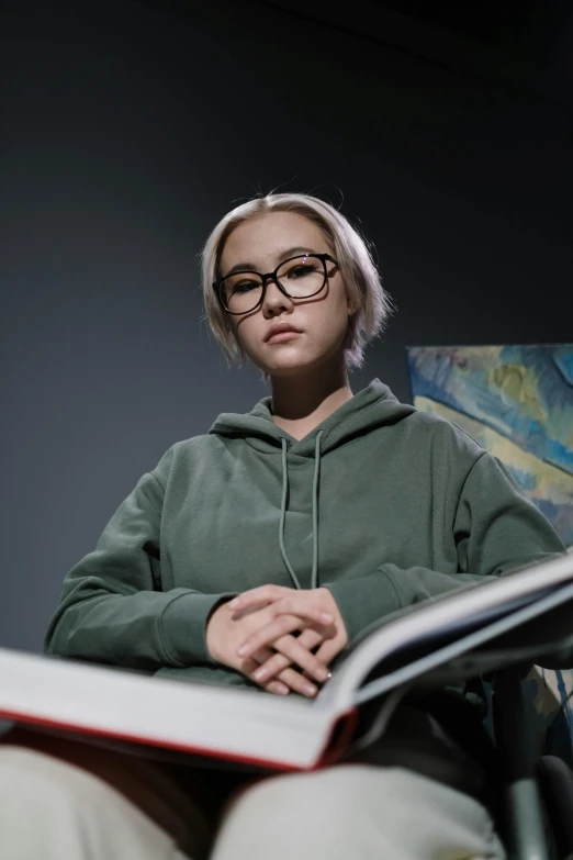 a woman sitting in a chair reading a book, inspired by Zhang Xiaogang, featured on reddit, hyperrealism, wearing medium - sized glasses, wearing a hoodie and sweatpants, loish and ross tran, still from a live action movie