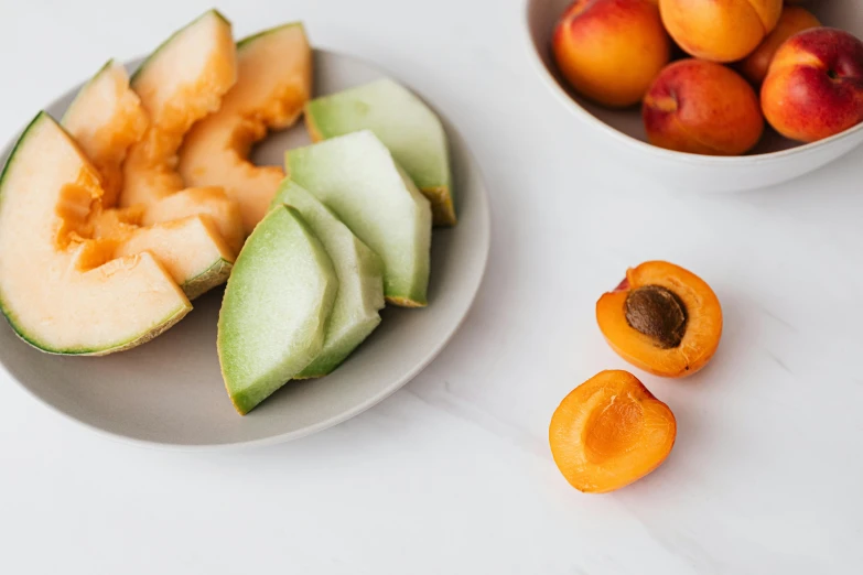 a white plate topped with sliced fruit next to a bowl of apricots, unsplash, wearing a melon, organic shapes, close-up product photo, background image