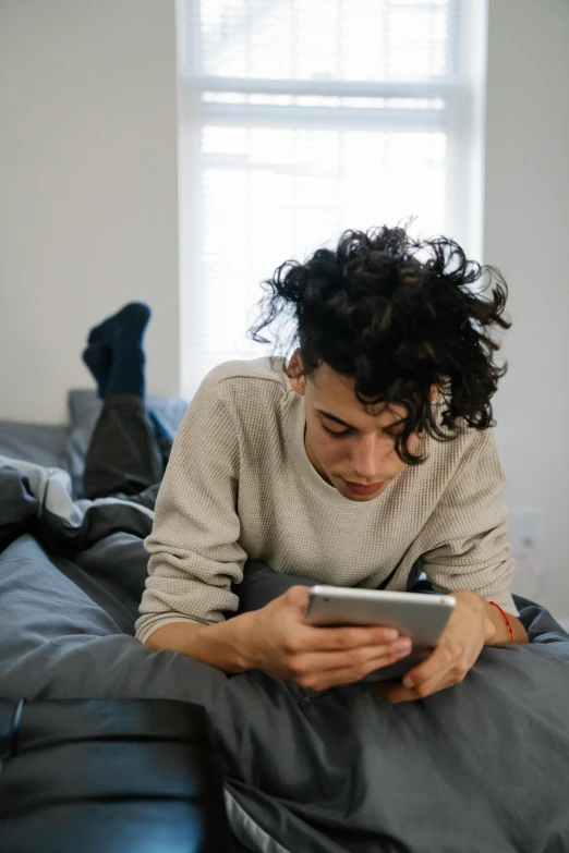 a man laying on a bed using a tablet computer, trending on pexels, renaissance, finn wolfhard, queer woman, checking her phone, curls