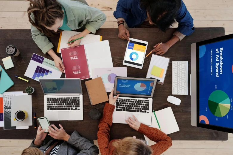 a group of people sitting around a table with laptops, trending on pexels, renaissance, 9 9 designs, school curriculum expert, a high angle shot, multicoloured