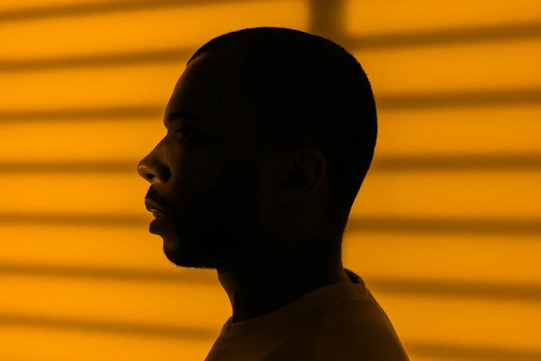 a man standing in front of a yellow wall, an album cover, inspired by Theo Constanté, profile image, orange light, tyler, backlighted