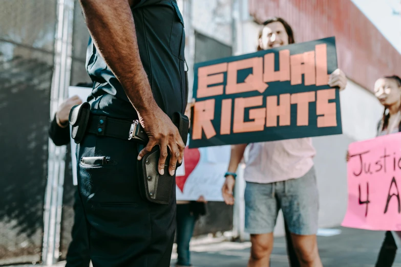 a man holding a sign that says equal rights, by Julia Pishtar, trending on pexels, black arts movement, policeman closeup, shot from the side, lgbt, schools