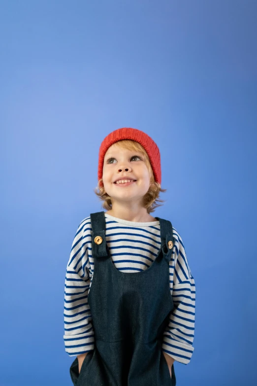 a little boy wearing overalls and a red hat, an album cover, pexels, blue background colour, french girl, beanie hat, high res photograph