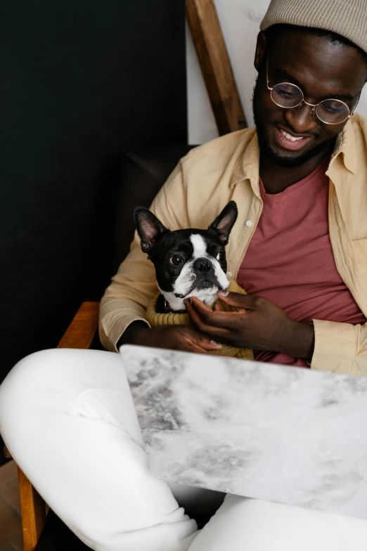 a man sitting in a chair holding a dog, by Cosmo Alexander, trending on pexels, man is with black skin, sitting on a mocha-colored table, french bulldog, 1 2 9 7