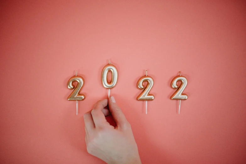 a person holding a candle in the shape of a number, by Emma Andijewska, trending on pexels, happening, year 2 0 2 2, pink background, holding a gold! cane!, candles!