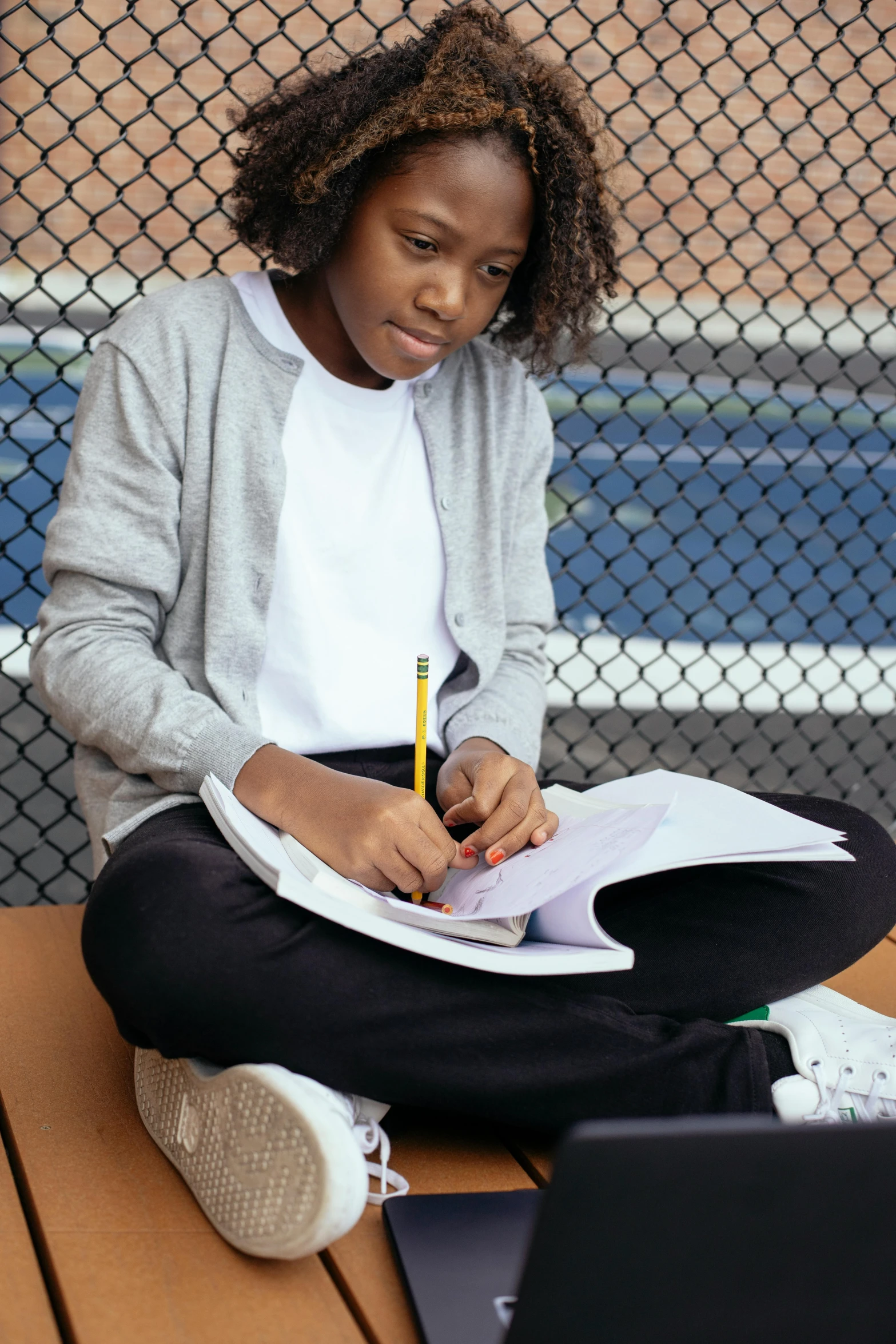 a woman sitting on a bench with a laptop and notebook, academic art, black teenage boy, on medium grade paper, sports setting, promo image