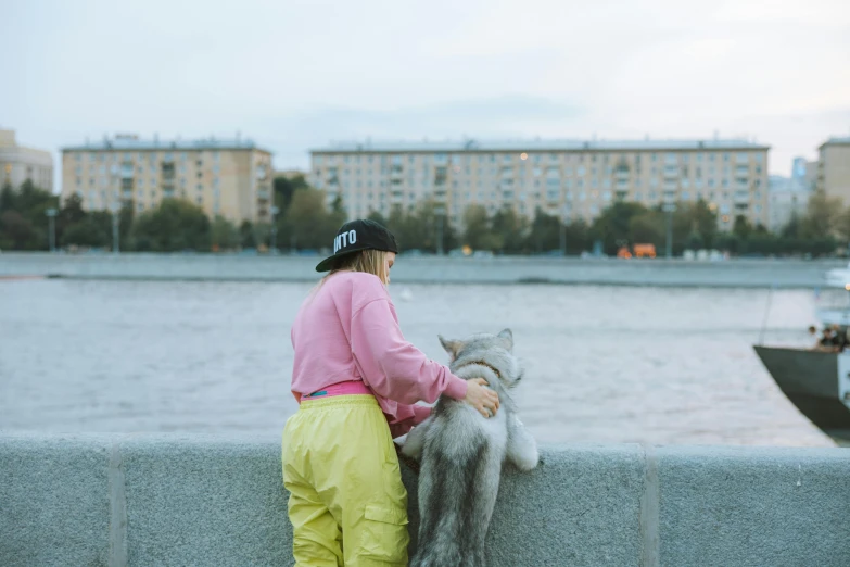 a person leaning on a wall next to a body of water, by Julia Pishtar, pexels contest winner, furry art, in moscow centre, best friends, pink, with yellow cloths