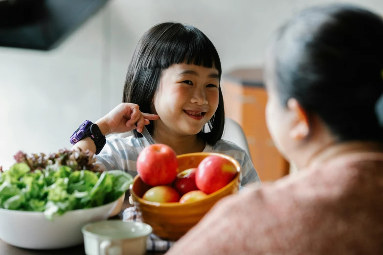 a little girl sitting at a table with a bowl of fruit, pexels contest winner, asian woman, being delighted and cheerful, profile image, medium shot of two characters