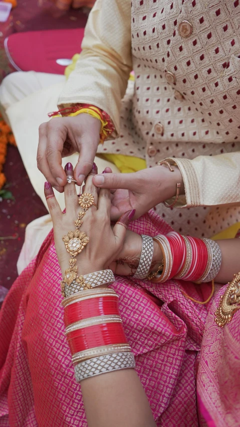 a close up of a person putting a ring on another person's finger, wearing a sari, thumbnail, pink and gold, embellishment