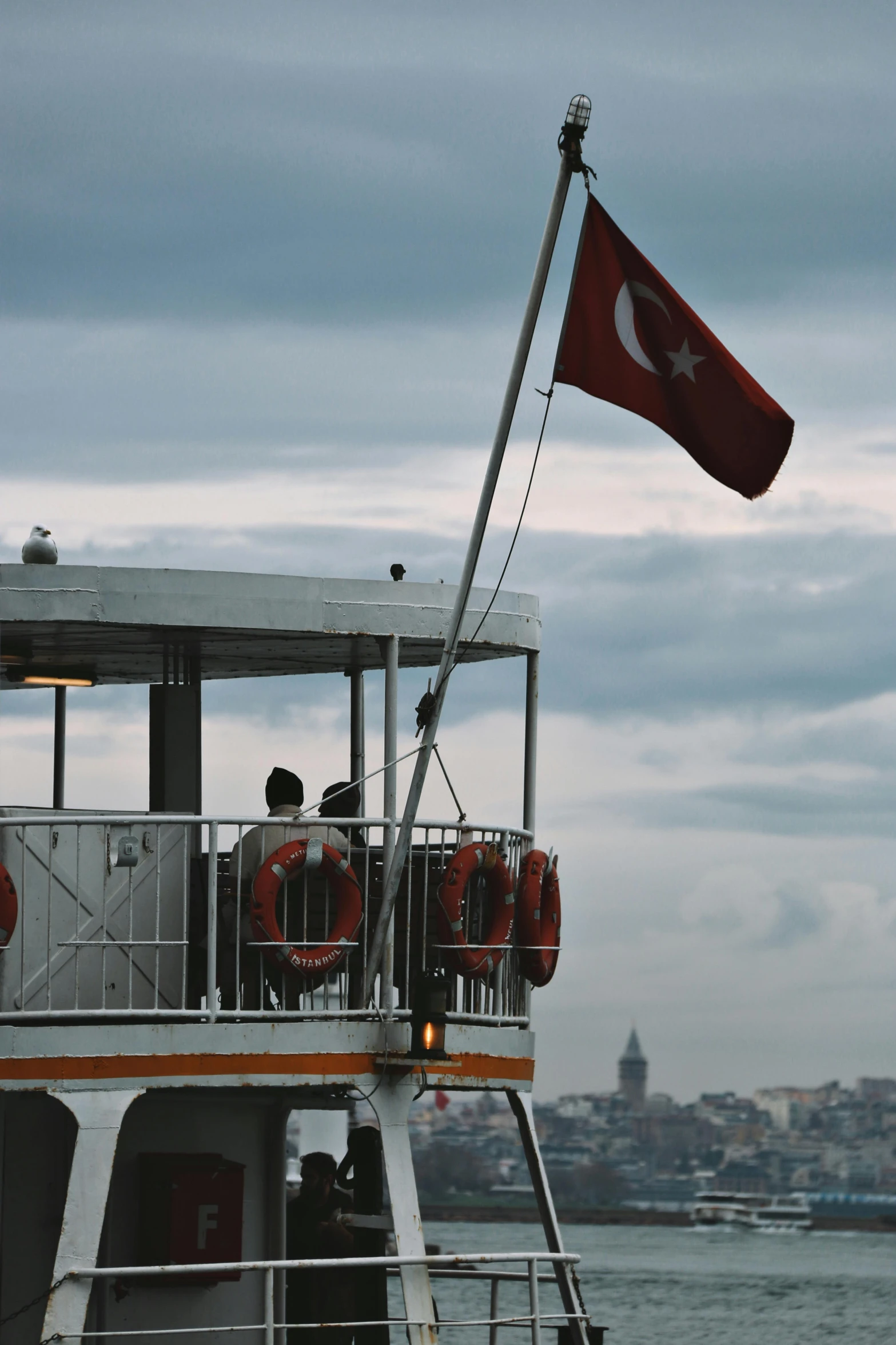 a boat that is sitting in the water, by Niyazi Selimoglu, hurufiyya, flag, observation deck, over the shoulder, close - up profile