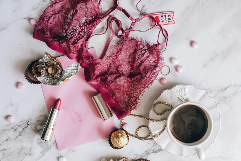 a pink bra top sitting on top of a table next to a cup of coffee, a photo, by Emma Andijewska, trending on pexels, aestheticism, ornate dark red opulent clothing, a messy, dressed in a lacy, posing together in bra