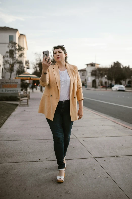 a woman walking down a sidewalk talking on a cell phone, a picture, trending on pexels, renaissance, plus size, yellow hue, wearing a blazer, mirror selfie