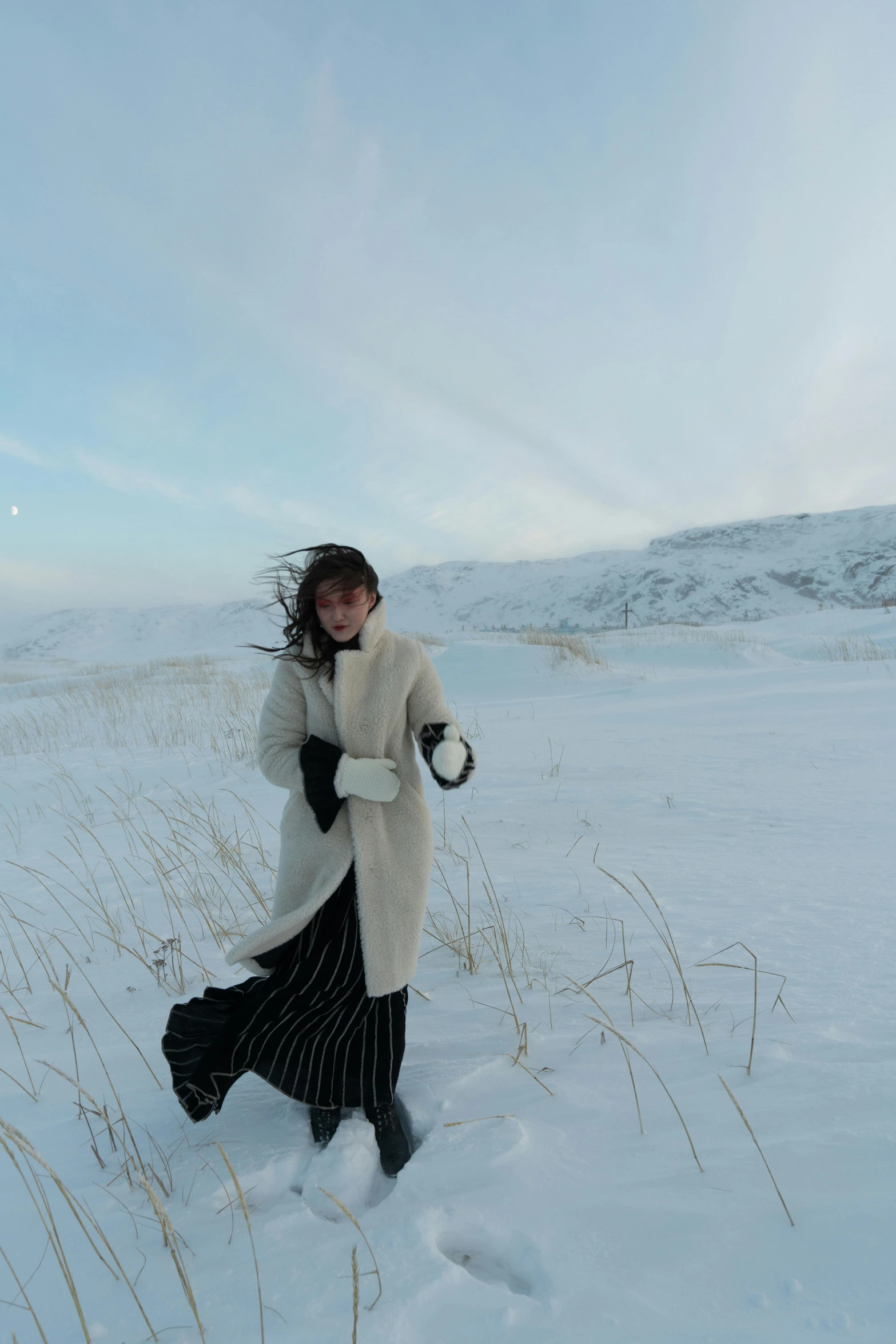 a woman walking across a snow covered field, inspired by Nína Tryggvadóttir, striking a pose, with rolling hills, ☁🌪🌙👩🏾, low quality photo