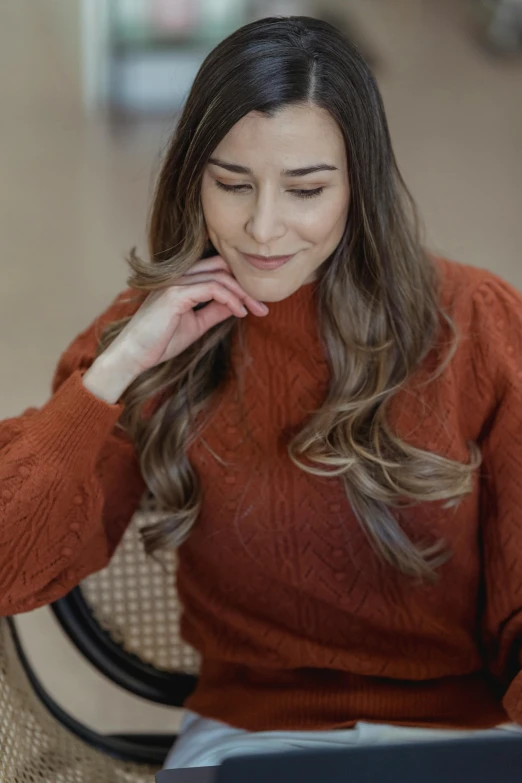 a woman sitting in front of a laptop computer, trending on pexels, renaissance, brown sweater, long wavy brown hair, orange hue, portrait mode photo