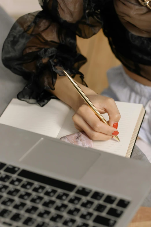 a woman writing in a notebook next to a laptop, golden detailing, ad image, multiple details, black