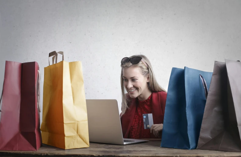 a woman sitting at a table with shopping bags and a laptop, pexels contest winner, very funny, avatar image, opening shot, thumbnail