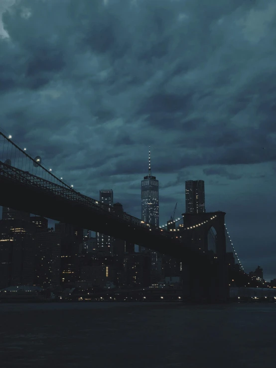 a bridge over a body of water under a cloudy sky, inspired by Elsa Bleda, unsplash contest winner, nighttime in gotham city, ☁🌪🌙👩🏾, new york buildings, ominous gothic aesthetic