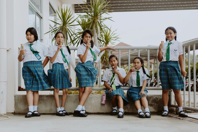 a group of young girls standing next to each other, pexels contest winner, ashcan school, in style of thawan duchanee, avatar image, girl wearing uniform, sit on a bench