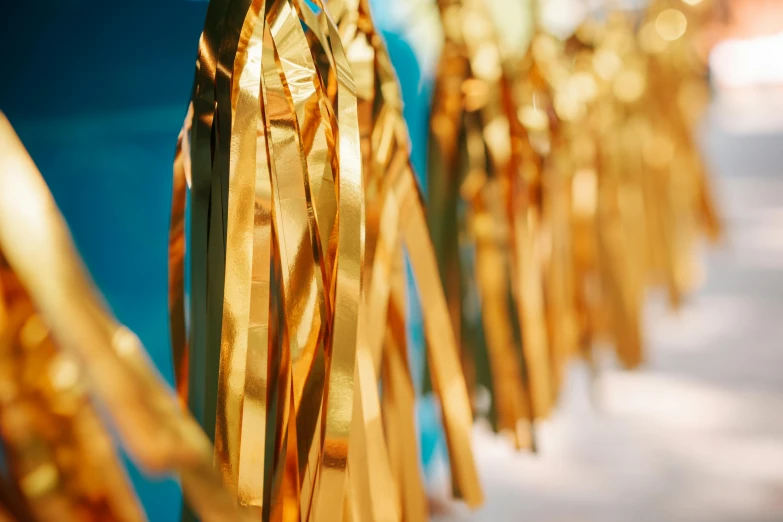 a row of gold tassels hanging from a string, by Julia Pishtar, pexels, process art, blue and yellow ribbons, turquoise gold details, shiny crisp finish, stylized photo