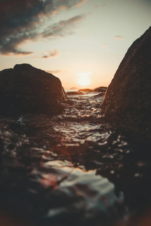 a sunset over a body of water with rocks in the foreground, by Jesper Knudsen, happening, cinematic closeup, high quality image, multiple stories, rough water