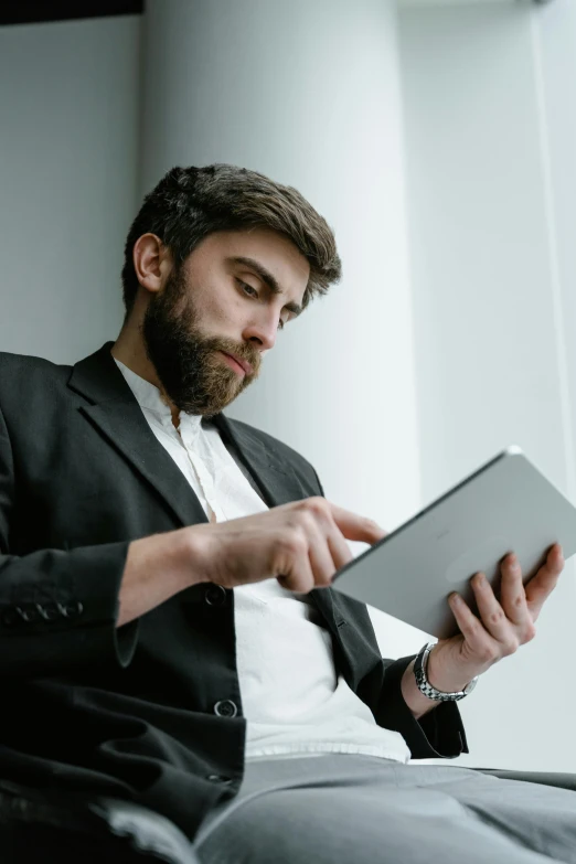 a man sitting in a chair using a tablet computer, pexels contest winner, with a beard and a black jacket, wearing a white button up shirt, standing, concentrated look