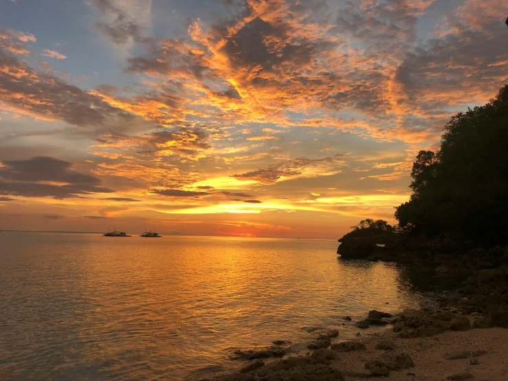 a sunset over a body of water with a boat in the distance, standing on a beach in boracay, slide show, landscape photo