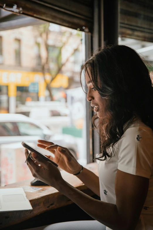 a woman sitting at a table looking at her phone, pexels contest winner, happening, looking through a window frame, woman with black hair, customers, using a magical tablet