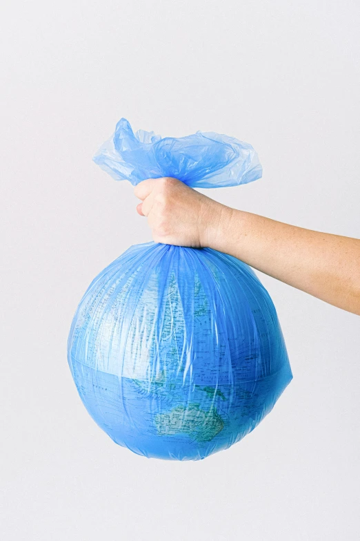 a person holding a blue bag of garbage, large globe, half turned around, made of silk paper, ready to eat