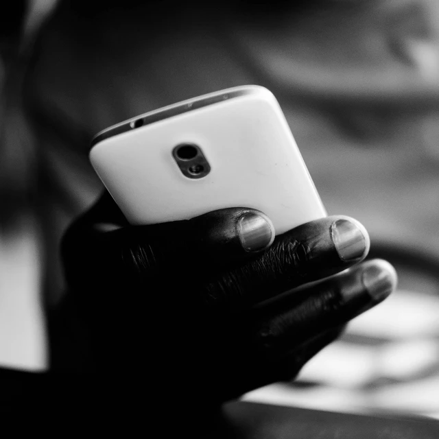a close up of a person holding a cell phone, a black and white photo, by Daniel Gelon, black main color, finger, item, black skin