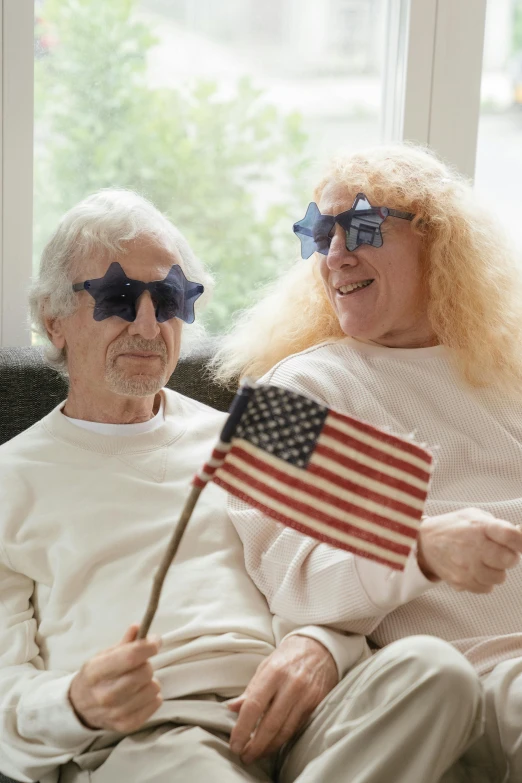 a man and a woman sitting on a couch holding american flags, trending on reddit, funny sunglasses, curly white hair, ( ( theatrical ) ), nursing home