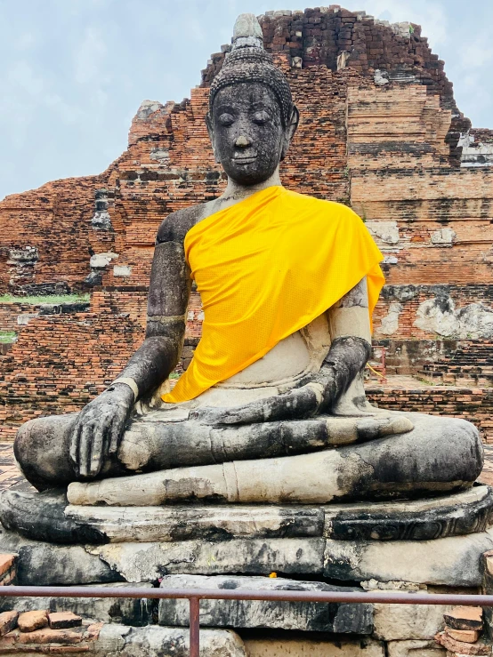 a buddha statue sitting on top of a pile of rubble, yellow robes, beautiful ancient ruins behind, 2019 trending photo