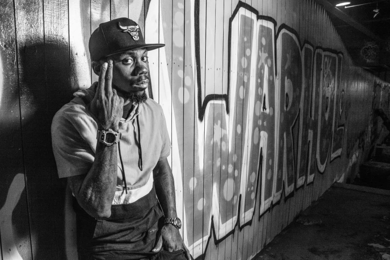 a black and white photo of a man leaning against a wall, inspired by Charles Martin, graffiti, snoop dogg, avatar for website, sitting down, lil wayne