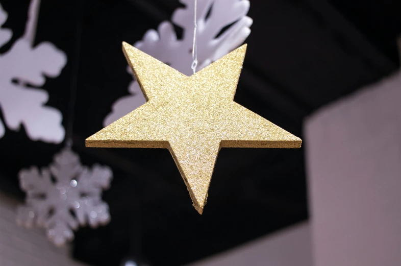 a gold star ornament hanging from a ceiling, a stipple, by Robbie Trevino, wooden decoration, foam, plain, glitter