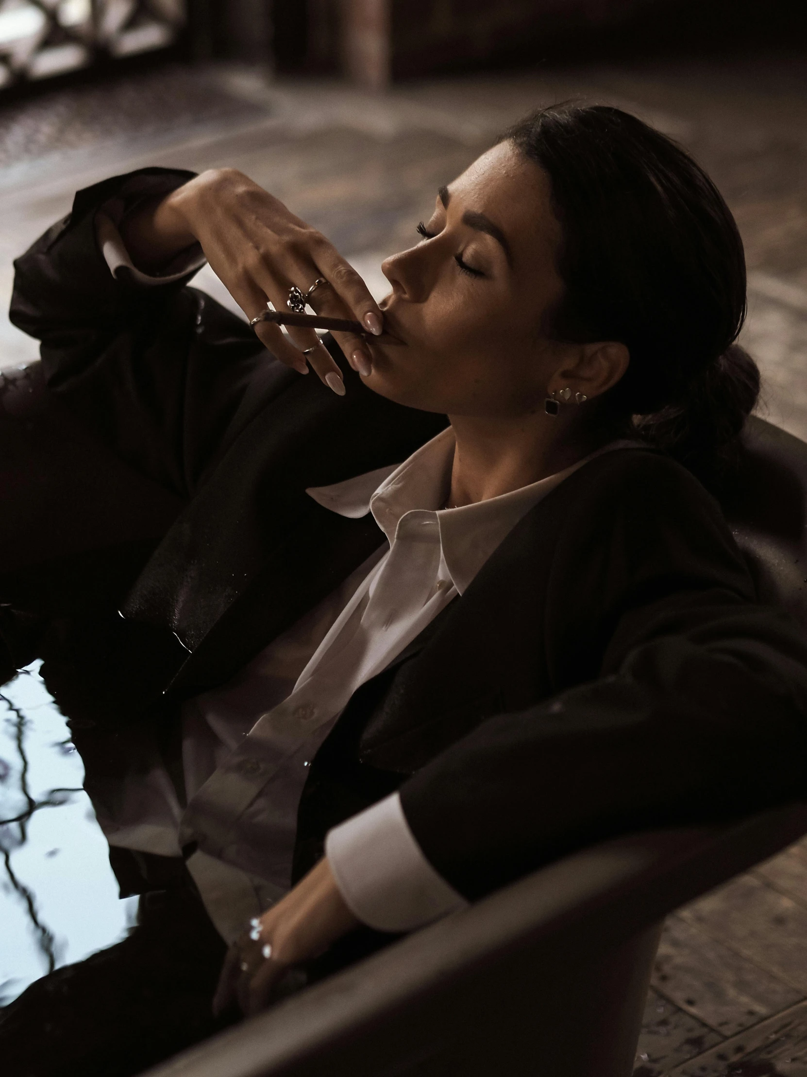 a woman sitting in a chair smoking a cigarette, trending on unsplash, hyperrealism, wearing a worn out suit, slicked black hair, laying down, ( ( theatrical ) )