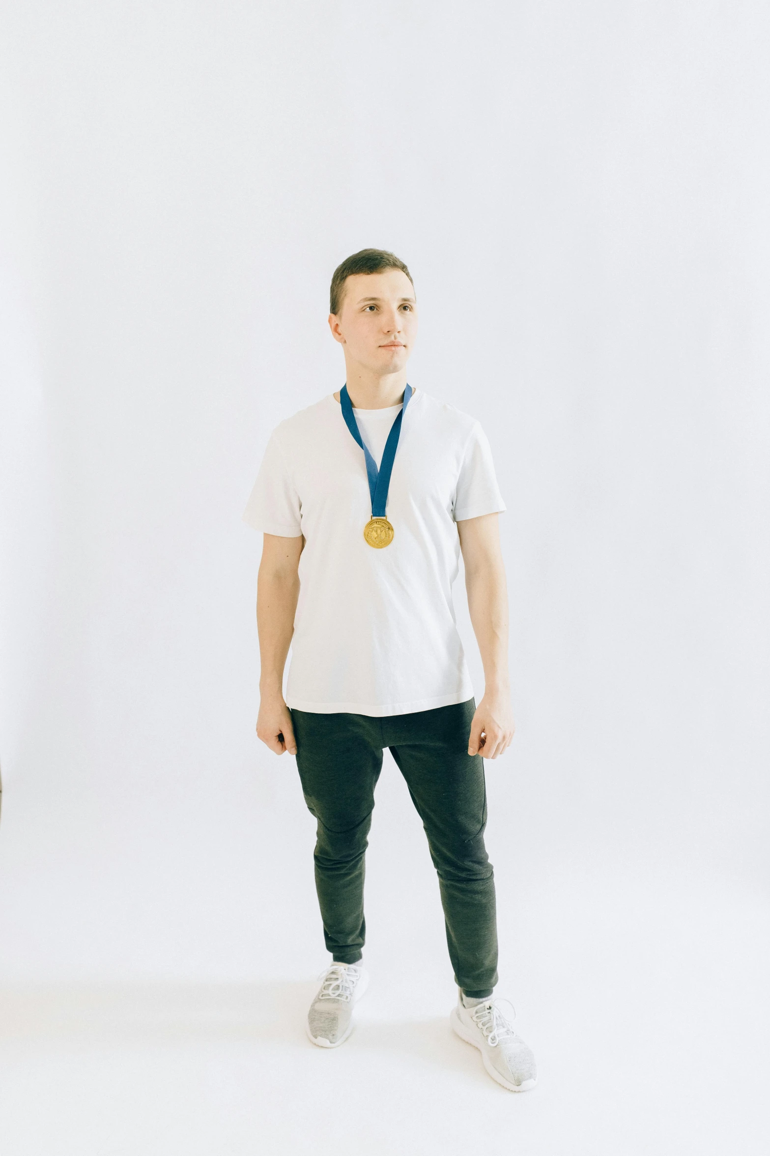 a man standing in front of a camera with a medal around his neck, inspired by Ryan Pancoast, pexels contest winner, plain white background, wearing pants and a t-shirt, andrea savchenko, profile image