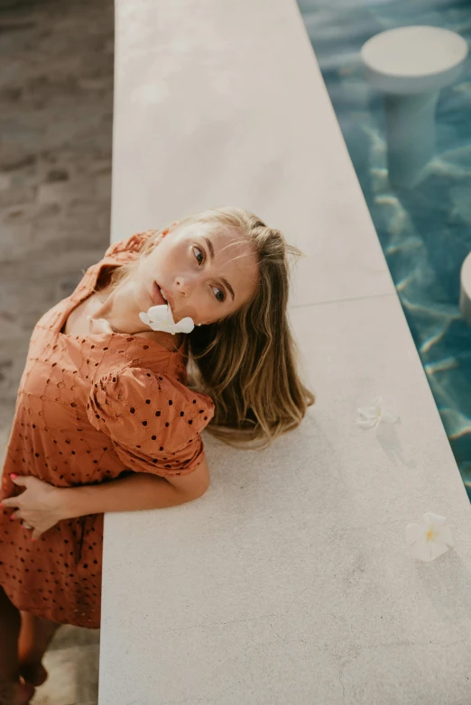 a woman leaning against a wall next to a pool, unsplash contest winner, sydney sweeney, robe. perfect faces, coral, high angle shot