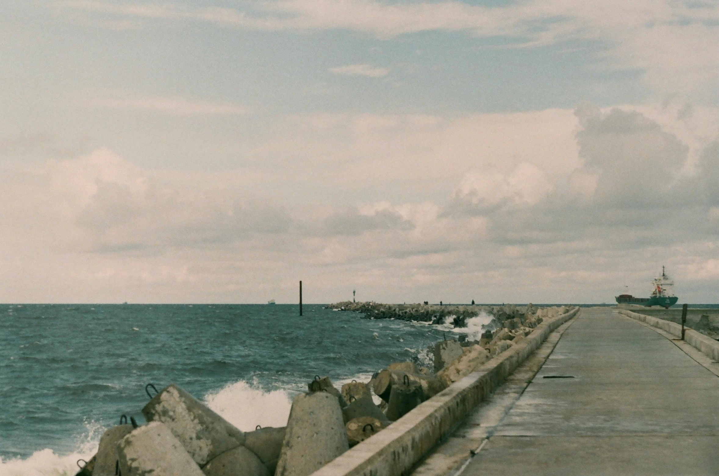 a man riding a skateboard down a sidewalk next to the ocean, a picture, unsplash, happening, near a jetty, vintage color, rocky seashore, harbour